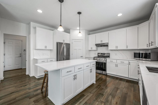 7804 Stafford Trl, Savage, MN 55378 - kitchen featuring appliances with stainless steel finishes, under cabinet range hood, dark wood-style floors, a center island, and tasteful backsplash