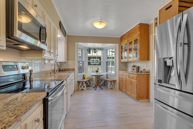 426 Armstrong Ave, Litchfield, MN 55355 - kitchen featuring appliances with stainless steel finishes, decorative backsplash, brown cabinets, light stone countertops, and glass insert cabinets