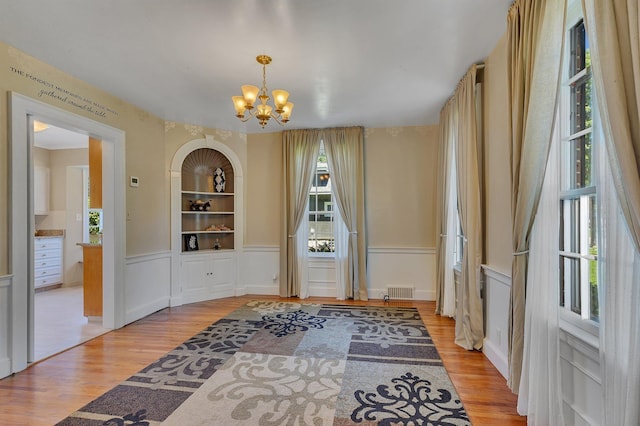 426 Armstrong Ave, Litchfield, MN 55355 - unfurnished dining area featuring a chandelier, light wood-style floors, wainscoting, a decorative wall, and built in shelves