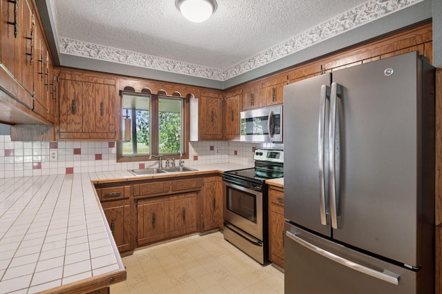 29908 108th St NW, Baldwin Twp, MN 55371 - kitchen with stainless steel appliances, tile counters, a textured ceiling, brown cabinets, and decorative backsplash