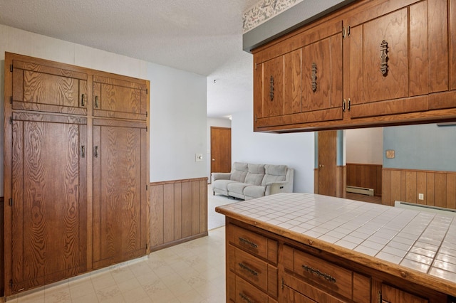29908 108th St NW, Baldwin Twp, MN 55371 - kitchen with tile countertops, wainscoting, wood walls, a textured ceiling, and brown cabinetry