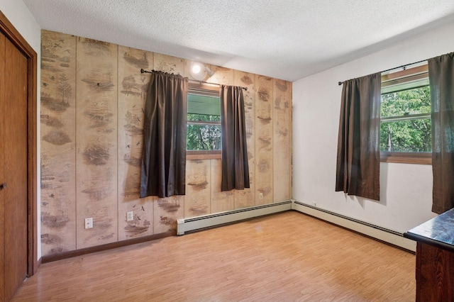 29908 108th St NW, Baldwin Twp, MN 55371 - spare room with light wood-type flooring, a textured ceiling, a baseboard heating unit, and wooden walls
