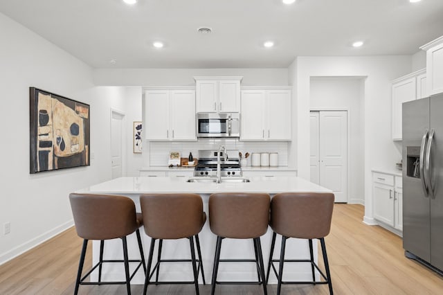 3907 Helena Ave N, Oakdale, MN 55128 - kitchen featuring stainless steel appliances, light wood-style floors, a kitchen breakfast bar, white cabinetry, and recessed lighting