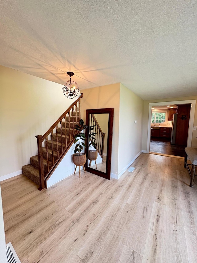 2812 150th St, Maxwell Twp, MN 56232 - unfurnished living room featuring a textured ceiling, wood finished floors, stairway, and a chandelier
