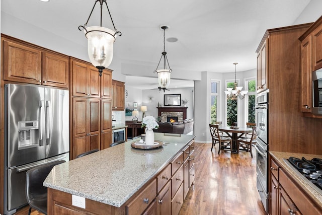 12346 Harvard Ave, Eden Prairie, MN 55347 - kitchen with stainless steel appliances, a fireplace, wood finished floors, brown cabinets, and light stone counters