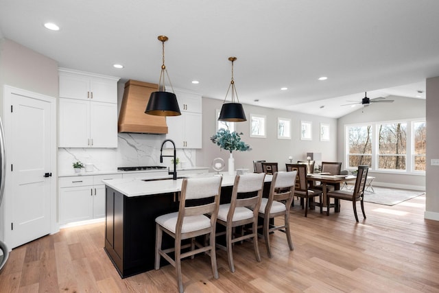 7617 Ocean Ave NE, Otsego, MN 55330 - kitchen with custom range hood, light wood-style flooring, a center island with sink, tasteful backsplash, and white cabinets