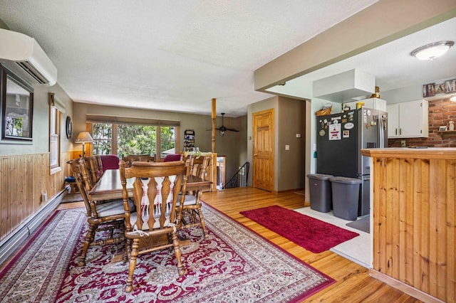 4745 Patterson Trl, Brainerd, MN 56401 - dining room featuring a wall unit AC, wood finished floors, a textured ceiling, a baseboard heating unit, and wainscoting