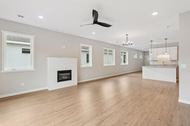 2728 229th Ln NW, Saint Francis, MN 55070 - unfurnished living room featuring a ceiling fan, recessed lighting, a glass covered fireplace, a chandelier, and light wood-type flooring