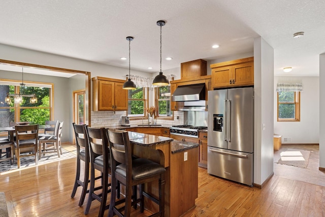 11985 Lever Ct NE, Blaine, MN 55449 - kitchen with appliances with stainless steel finishes, brown cabinetry, wall chimney exhaust hood, dark stone counters, and backsplash
