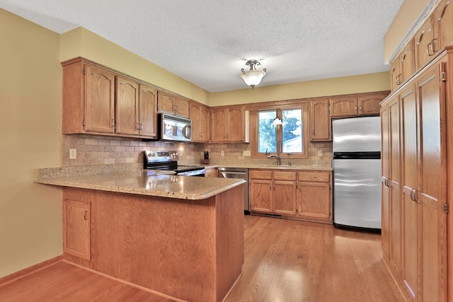 6 Pleasant View Ln, Circle Pines, MN 55014 - kitchen with appliances with stainless steel finishes, a peninsula, light wood finished floors, decorative backsplash, and a textured ceiling