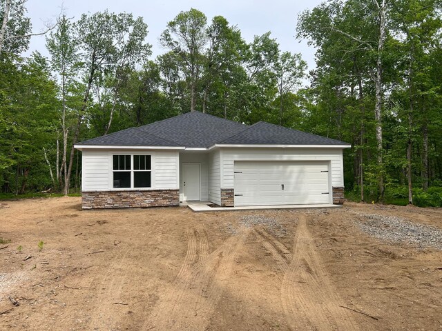 view of front of home featuring stone siding, driveway, a garage, and roof with shingles