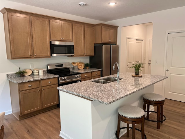 kitchen featuring stainless steel appliances, dark wood finished floors, a breakfast bar area, and light stone countertops