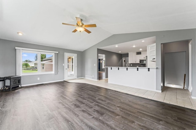2100 10th St SW, Austin, MN 55912 - unfurnished living room featuring light wood finished floors, ceiling fan, vaulted ceiling, and a wood stove