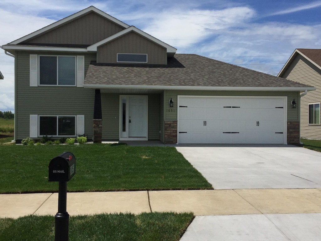 1051 Yellowstone Ave, Saint Cloud, MN 56303 - view of front facade with a garage, a front yard, driveway, a shingled roof, and stone siding