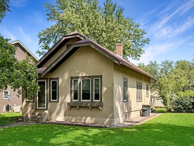 306 Jefferson St, Minneota, MN 56264 - back of house featuring stucco siding, entry steps, a lawn, and a chimney