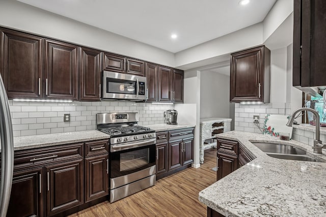 8 110th Ln NW, Coon Rapids, MN 55448 - kitchen with appliances with stainless steel finishes, light wood-style flooring, dark brown cabinetry, light stone countertops, and backsplash