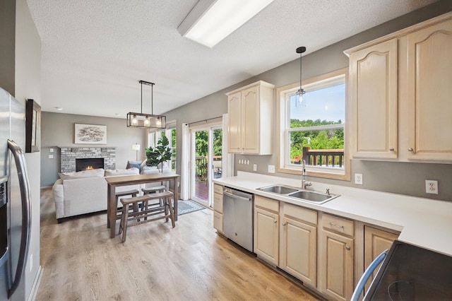 2722 Autumn Woods Dr, Chaska, MN 55318 - kitchen featuring appliances with stainless steel finishes, a lit fireplace, a textured ceiling, pendant lighting, and light wood-style flooring