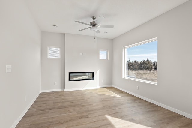39726 Fallbrook Ave, North Branch, MN 55056 - unfurnished living room featuring healthy amount of natural light, a glass covered fireplace, a ceiling fan, and light wood finished floors