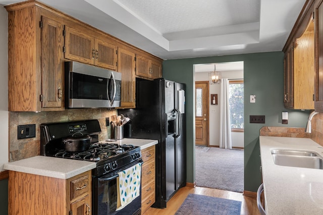 1322 Bidwell St, West Saint Paul, MN 55118 - kitchen featuring black appliances, a tray ceiling, light countertops, brown cabinets, and light wood-style flooring