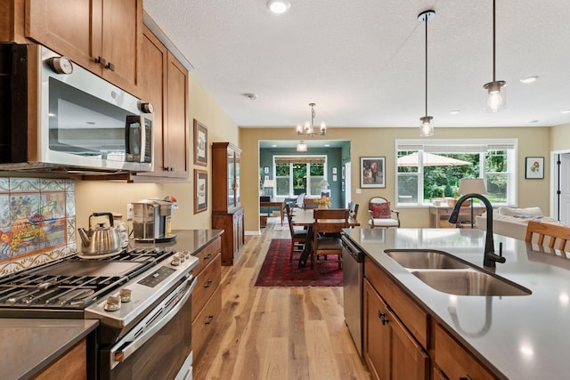 1101 Fabel Ln, Waconia, MN 55387 - kitchen with appliances with stainless steel finishes, light wood-style floors, brown cabinets, hanging light fixtures, and dark countertops