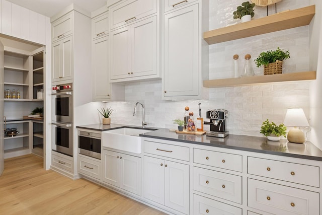 6176 Broadview Ave, Credit River Twp, MN 55372 - kitchen with open shelves, stainless steel double oven, dark countertops, light wood-style floors, and decorative backsplash