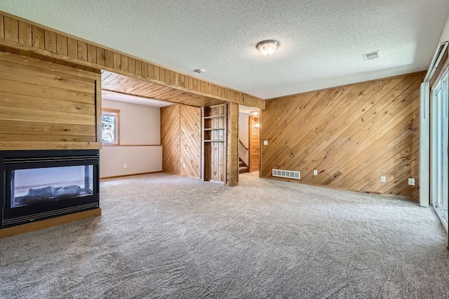 703 11th Ave SW, Isanti, MN 55040 - unfurnished living room featuring wood walls, stairs, carpet flooring, a textured ceiling, and a multi sided fireplace