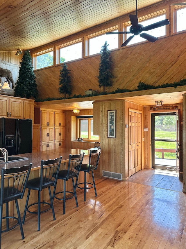 1938 Pine Cliff Rd NW, Walker, MN 56484 - kitchen featuring black fridge with ice dispenser, wooden walls, high vaulted ceiling, a ceiling fan, and a kitchen breakfast bar