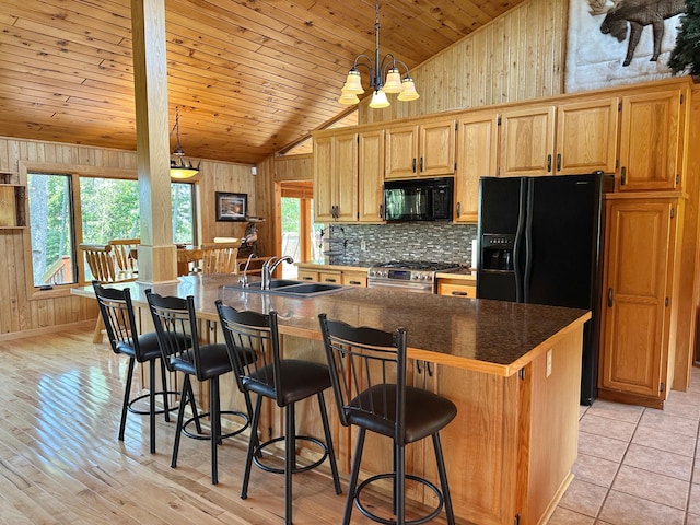 1938 Pine Cliff Rd NW, Walker, MN 56484 - kitchen featuring black appliances, wooden walls, dark countertops, a kitchen island with sink, and high vaulted ceiling