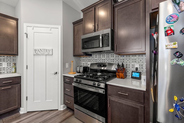 4617 Cobalt Ln, Woodbury, MN 55129 - kitchen with appliances with stainless steel finishes, wood finished floors, dark brown cabinetry, light countertops, and decorative backsplash