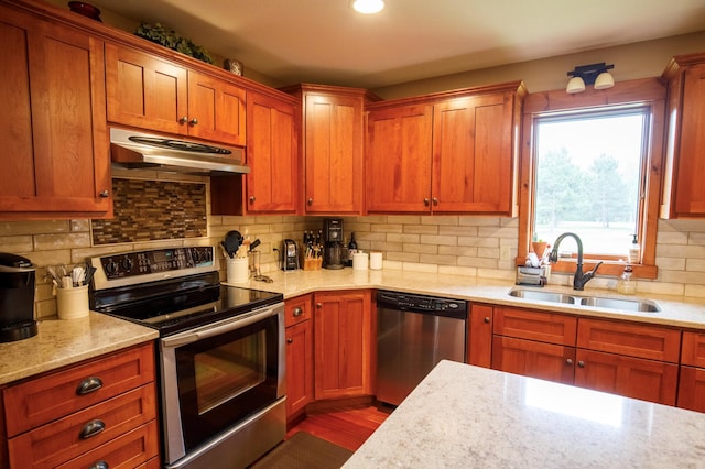 32433 Cedar St, Breezy Point, MN 56472 - kitchen featuring appliances with stainless steel finishes, under cabinet range hood, backsplash, light stone countertops, and brown cabinetry