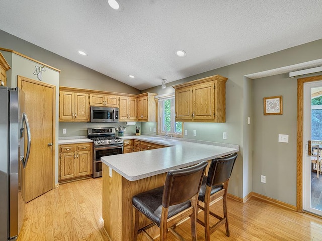 1483 Woods Creek Dr, Delano, MN 55328 - kitchen featuring appliances with stainless steel finishes, light countertops, light wood finished floors, a textured ceiling, and a kitchen breakfast bar