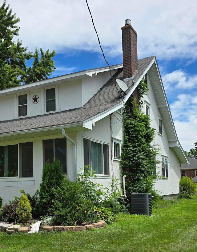 309 5th St SW, Austin, MN 55912 - view of side of property with a chimney, stucco siding, a yard, and roof with shingles
