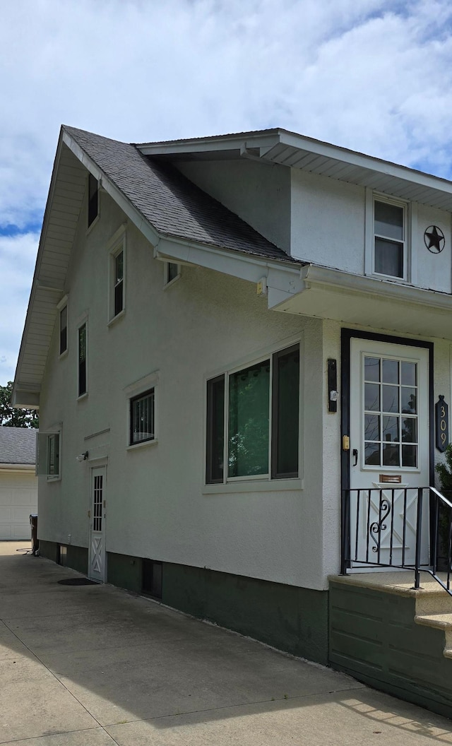 309 5th St SW, Austin, MN 55912 - view of side of property featuring stucco siding, a shingled roof, and a garage