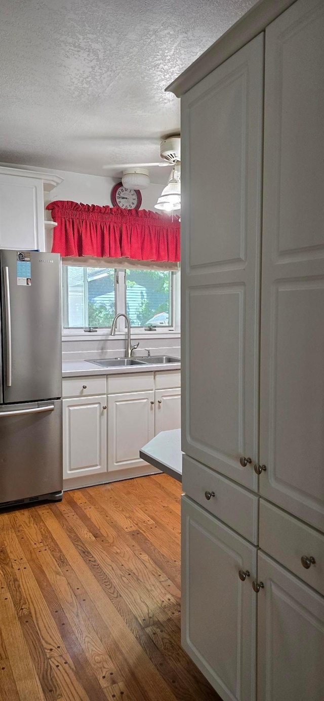 309 5th St SW, Austin, MN 55912 - kitchen with freestanding refrigerator, a textured ceiling, white cabinets, light wood-style flooring, and light countertops