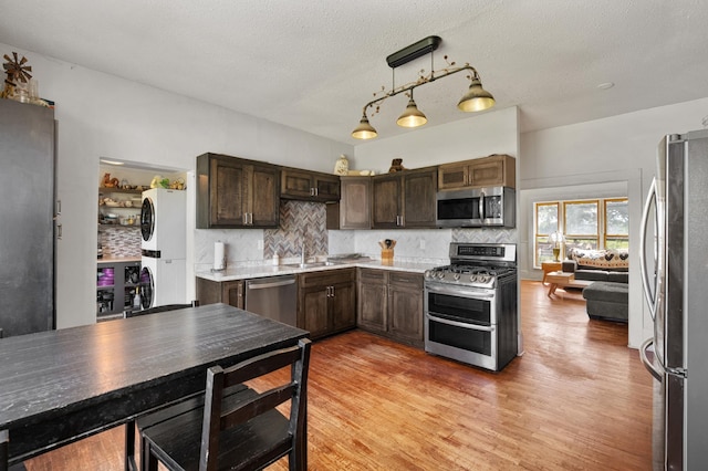 W2741 US Highway 10, Grant Twp, WI 54436 - kitchen featuring appliances with stainless steel finishes, stacked washer / dryer, dark brown cabinetry, tasteful backsplash, and light wood-type flooring