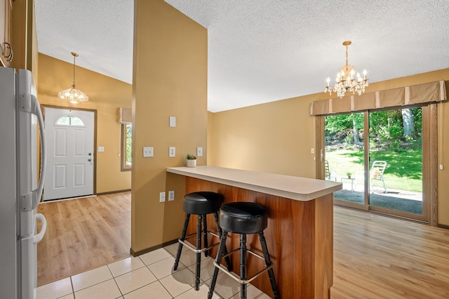 1010 Zanzibar Ln N, Plymouth, MN 55447 - kitchen with fridge, a chandelier, a peninsula, vaulted ceiling, and a textured ceiling