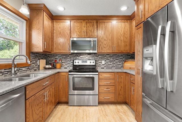 1602 19th Ave SW, Austin, MN 55912 - kitchen featuring stainless steel appliances, brown cabinetry, light wood-type flooring, light stone counters, and backsplash