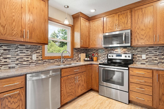 1602 19th Ave SW, Austin, MN 55912 - kitchen with stainless steel appliances, brown cabinetry, a textured ceiling, and light stone countertops
