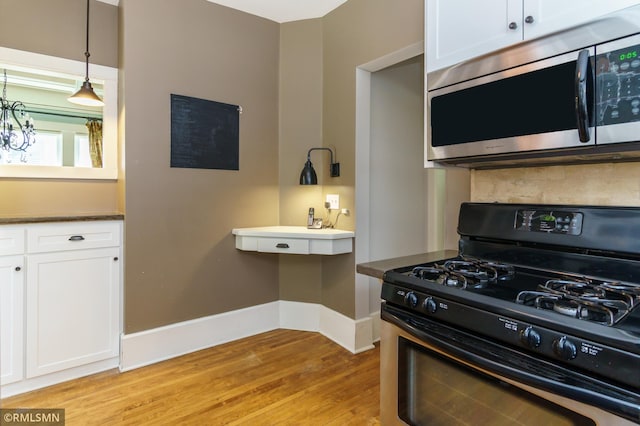4709 Colfax Ave S, Minneapolis, MN 55419 - kitchen featuring stainless steel microwave, black gas range oven, light wood-style floors, white cabinets, and hanging light fixtures