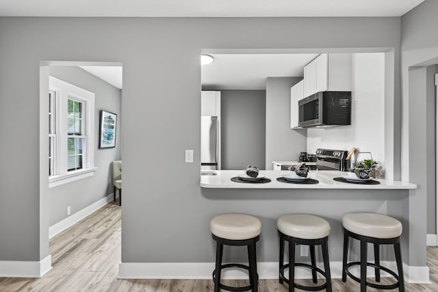 4301 Columbus Ave, Minneapolis, MN 55407 - kitchen with stainless steel appliances, white cabinetry, a kitchen breakfast bar, and light wood-style floors