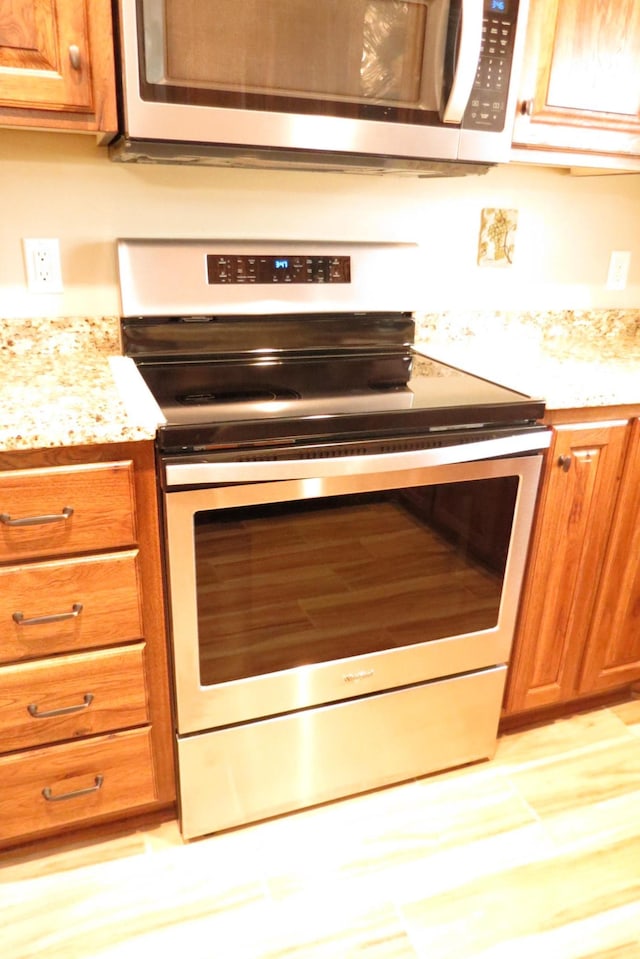 307 14th St N, Cold Spring, MN 56320 - kitchen view of stainless steel appliances, brown cabinetry, light stone counters, and light wood finished floors