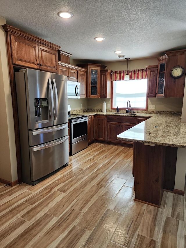 307 14th St N, Cold Spring, MN 56320 - kitchen featuring stainless steel appliances, a peninsula, light wood-style flooring, a textured ceiling, and glass insert cabinets
