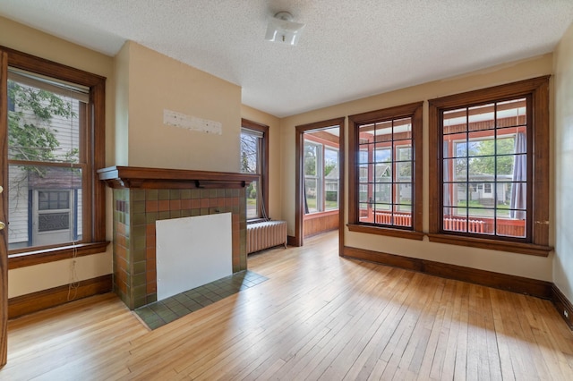 211 Saint Marie St, Duluth, MN 55803 - unfurnished living room with radiator, hardwood / wood-style floors, a textured ceiling, and a tiled fireplace