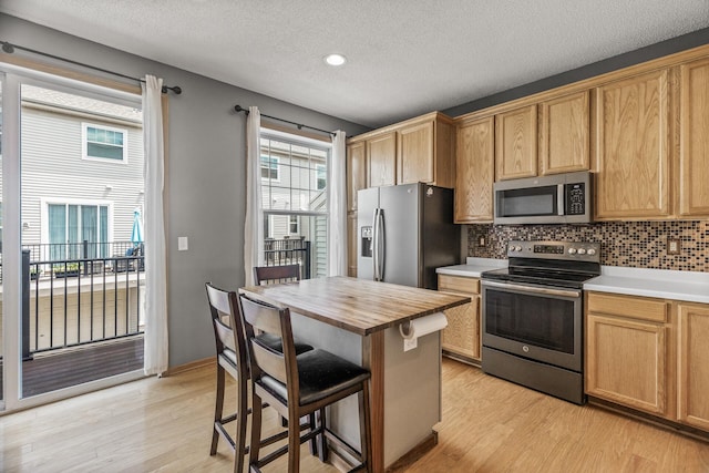 2079 Clover Ridge Dr, Chaska, MN 55318 - kitchen with appliances with stainless steel finishes, butcher block counters, light wood-style floors, a kitchen bar, and a textured ceiling