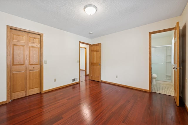 629 73rd Way N, Brooklyn Park, MN 55444 - unfurnished bedroom with dark wood-style flooring, a textured ceiling, and connected bathroom