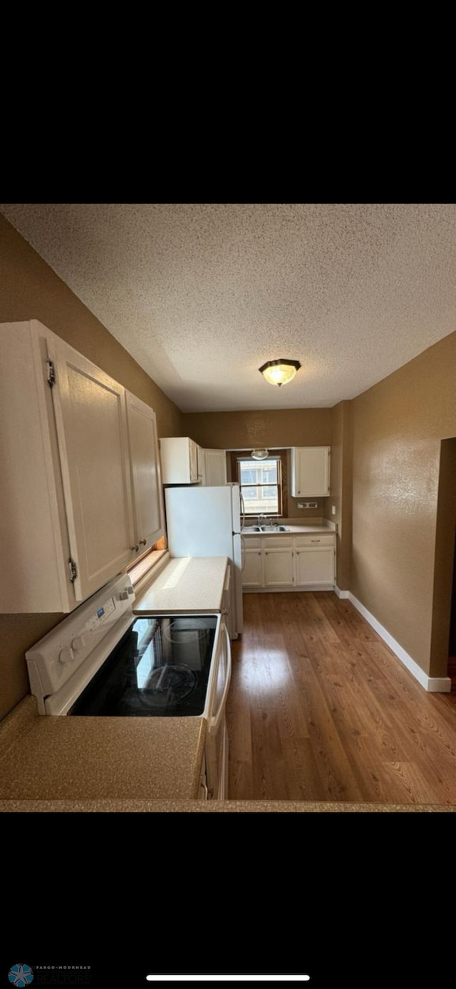 802 11th Ave N, Fargo, ND 58102 - kitchen with range with electric stovetop, light wood-style flooring, white cabinets, freestanding refrigerator, and a textured ceiling
