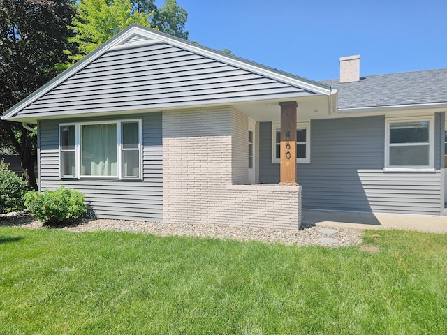 460 3rd St, Bird Island, MN 55310 - view of home's exterior featuring a chimney, a yard, brick siding, a shingled roof, and a porch