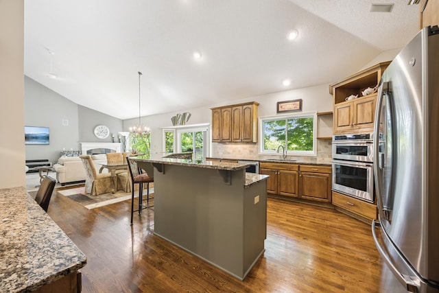 13703 47th St NE, Saint Michael, MN 55376 - kitchen with stainless steel appliances, lofted ceiling, a breakfast bar, tasteful backsplash, and brown cabinetry