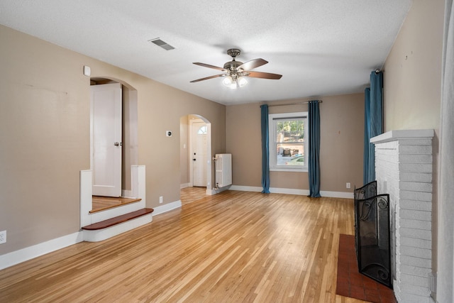 506 6th Ave SW, Austin, MN 55912 - unfurnished living room with radiator heating unit, arched walkways, a fireplace, ceiling fan, and light wood finished floors