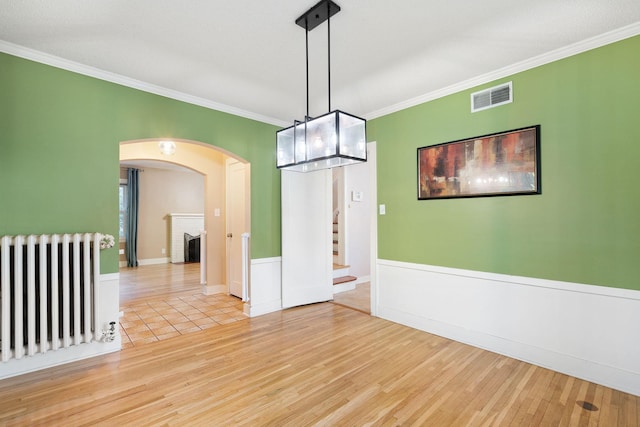506 6th Ave SW, Austin, MN 55912 - spare room featuring radiator, wood finished floors, crown molding, arched walkways, and stairway